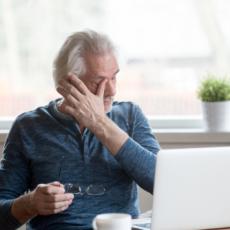 Image of older man in front of computer rubbing his eyes.