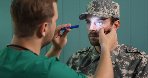 Image of Doctor shining light in man who is dressed in military uniforms's eye.