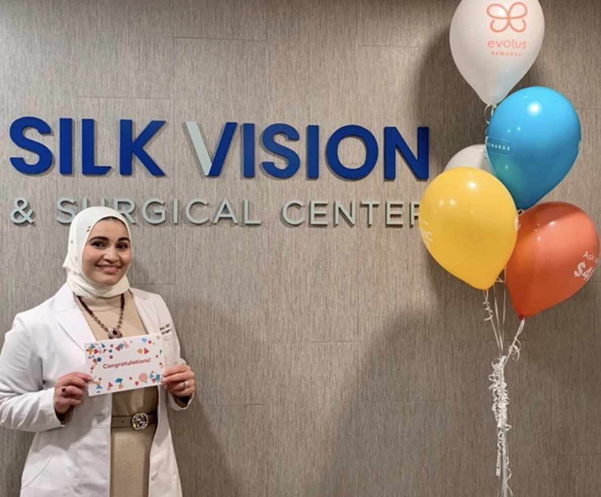 Dr. Rajjoub holds a sign saying "Congratulations" while standing in front of the Silk Vision lobby sign.