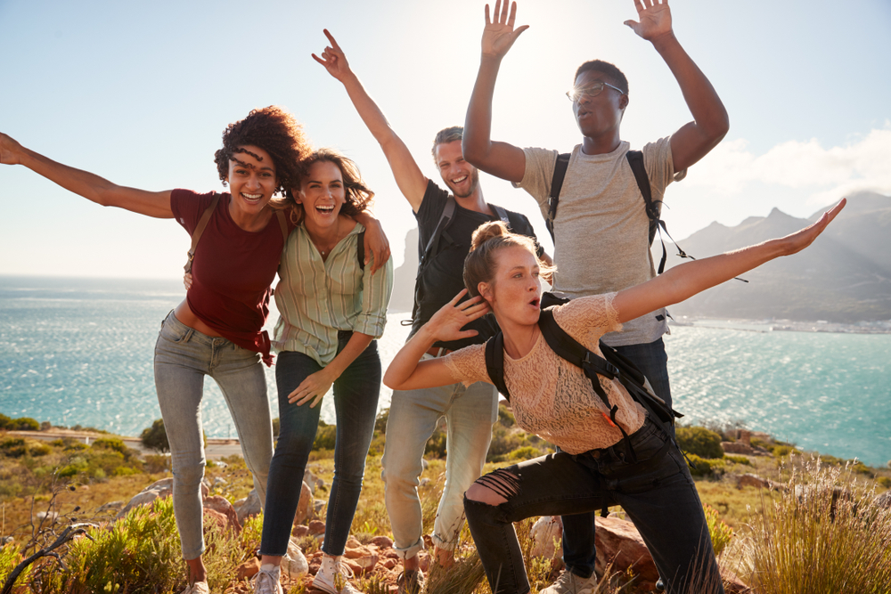 Millennials who had LASIK eye surgery are friends on a hiking trip celebrate reaching the summit and have fun posing for photos