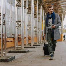 Man traveling with suitcase and nice attire wearing eyeglasses. Smiling. Checking his phone. The Importance of Traveling for the Best LASIK Surgeon